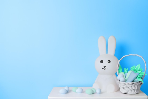 Lapin de Pâques jouet blanc, panier avec carottes jouets et oeufs de Pâques sur fond bleu