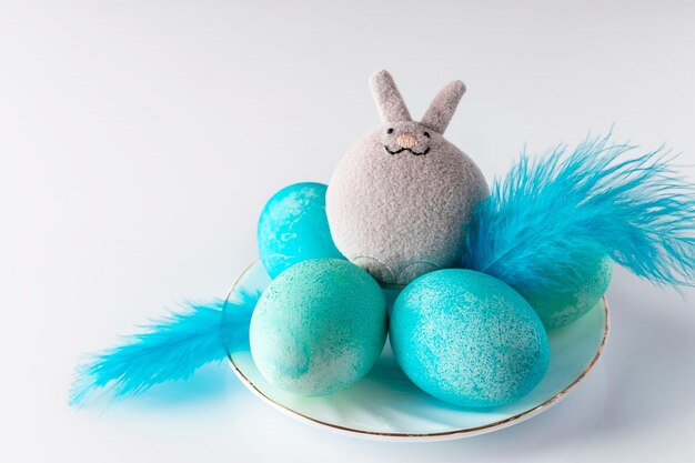 Lapin de Pâques jouet mignon et oeufs peints en bleu avec des plumes sur fond blanc Placez votre texte