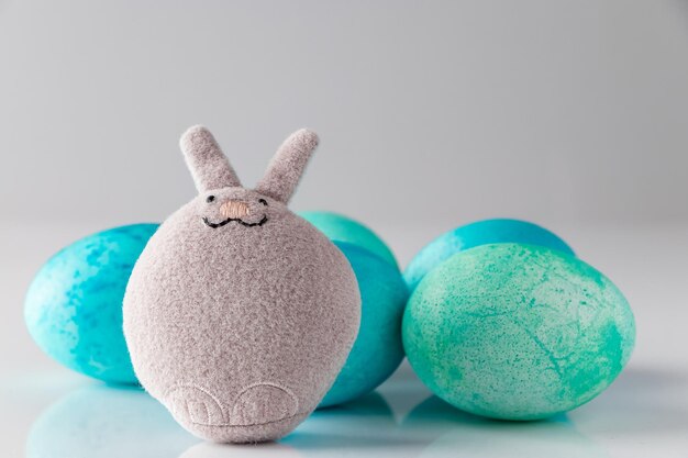 Lapin de Pâques jouet mignon et oeufs peints en bleu avec des plumes sur fond blanc Placez votre texte