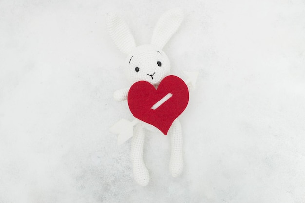 Un lapin tricoté blanc tient un coeur rouge sur fond gris