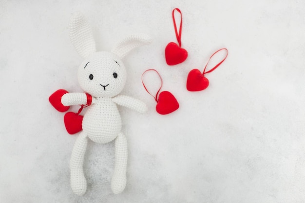 Un lapin tricoté blanc tient des coeurs rouges sur fond gris