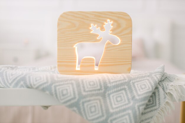 Lapms de nuit. Intérieur de la maison et décor cosy. Lampe en bois avec image découpée de cerf, sur table, dans une belle chambre lumineuse à la maison.