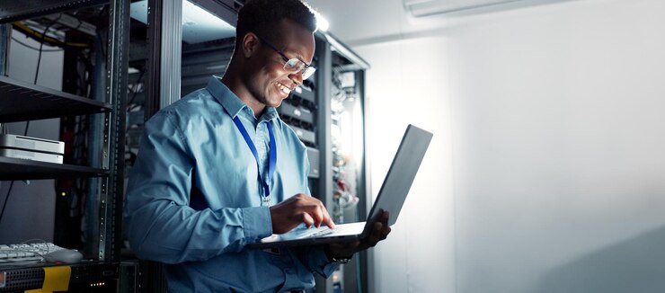 Photo laptop salle de serveur et homme noir sur le réseau pour la maintenance logiciel de programmation ou de frappe tech centre de données et ingénieur heureux sur la base de données du système pour la cybersécurité de l'information ou l'informatique en nuage