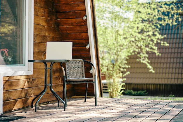 Laptop sur la table à café près de la chaise en tourbe sur la terrasse de la cabane en rondins Concept de travail à distance et indépendant