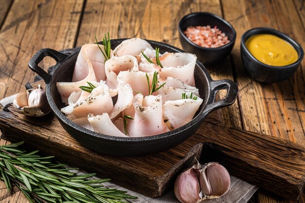 Lard frais tranché avec sel, ail et poivre dans une poêle avec des herbes. Fond en bois. Vue de dessus.