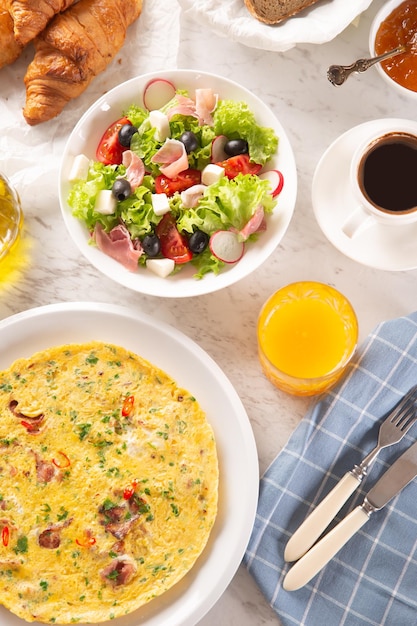 Large assortiment de plats, y compris omelette croissants salade pain café et jus d'orange servis sur une table