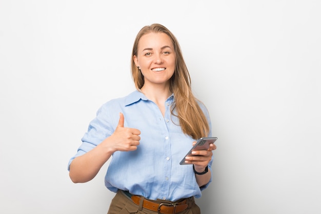 Une large femme d'affaires souriante tient un téléphone intelligent et montre le geste du pouce vers le haut.