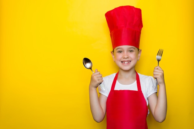 Large fille souriante en costume de chef rouge tenant une cuillère et une fourchette jaune