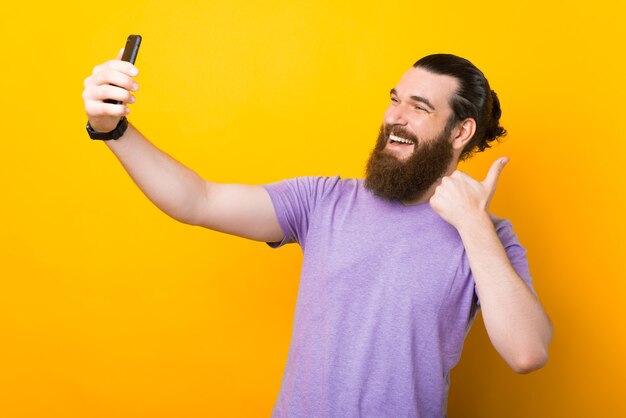 Large jeune homme souriant fait un selfie sur fond jaune.