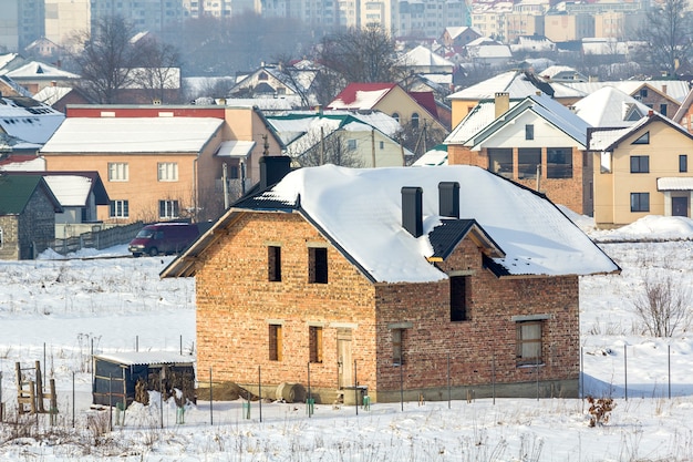 Large panorama hivernal de terrains ruraux à aménager dans un quartier résidentiel calme de banlieue. Nouvelle maison en brique non finie de village éloigné et de bâtiments de la haute ville sous un ciel bleu.