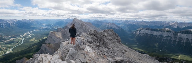 Large prise de vue panoramique d'une randonneuse profitant de la vue sur la vallée depuis le sommet de la montagne