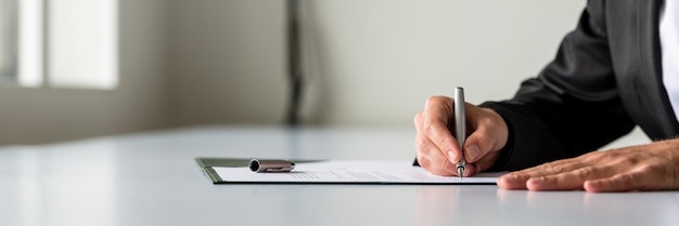 Photo large vue panoramique de la main de l'homme d'affaires signant un document juridique ou d'assurance ou un contrat commercial sur un bureau blanc.