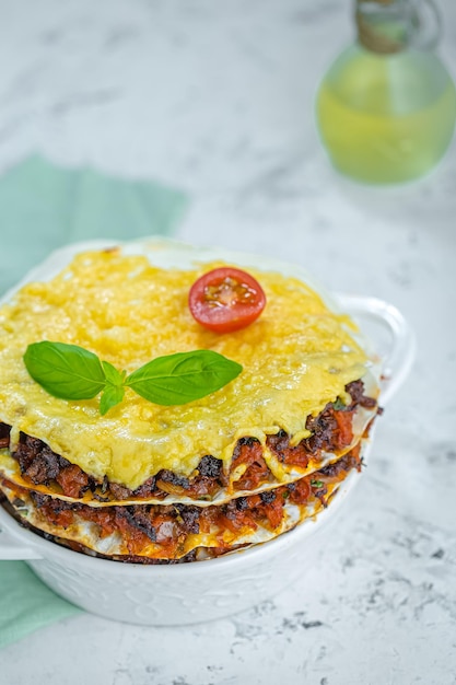 lasagne dans un pot d'argile rond et profond blanc, sur fond de marbre blanc, fourchette et couteau se trouvent sur un chiffon,