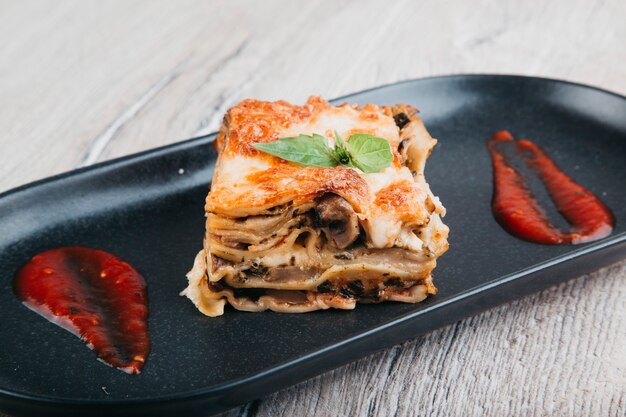 lasagne italienne à la sauce tomate sur une plaque noire et vue de dessus de fond en bois