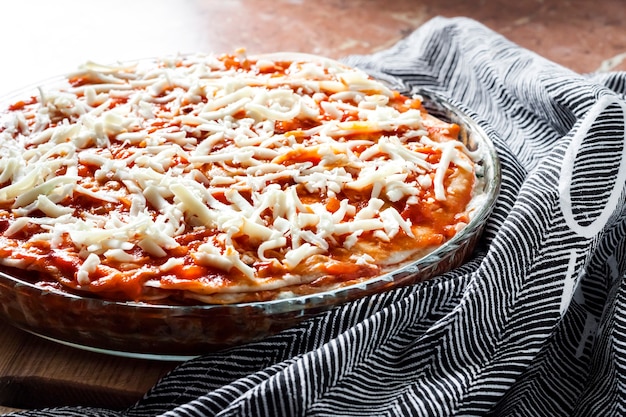 Lasagne maison prête pour la cuisson dans un plat de cuisson en verre rond sur planche de bois