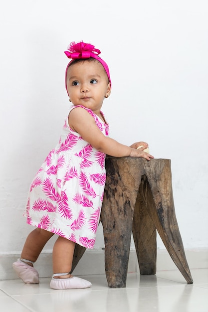 Latina baby girl debout à côté d'une chaise en bois avec une fille de fond blanc apprenant à marcher