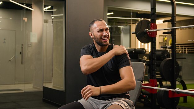 Photo latino ethnique multiracial américain homme fort assis dans le gymnase presse soulevez des haltères en haut du métal lourd