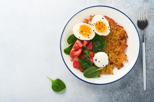 Latkes de pommes de terre au petit-déjeuner avec salade d'épinards à la crème sure, tomates et œufs durs sur fond clair Nourriture délicieuse pour le petit-déjeuner Vue de dessus