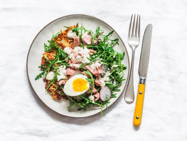 Latkes de pommes de terre et salade avec roquette thon en conserve œuf bouilli yaourt vinaigrette à la moutarde sur fond clair vue de dessus