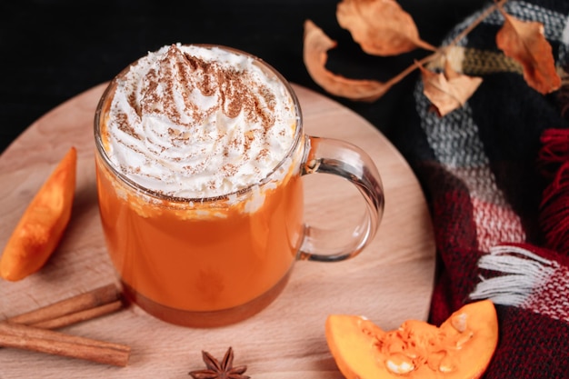 Latte de café à la citrouille avec de la crème fouettée sur fond sombre Boisson chaude d'automne avec de la cannelle et des épices dans une tasse en verre sur un plateau en bois