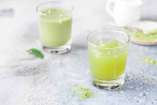 Latte vert Matcha glacé dans des verres avec de la poudre de matcha sur fond clair.