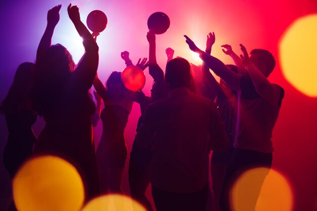 Lauder Une foule de personnes en silhouette lève les mains sur la piste de danse au néon