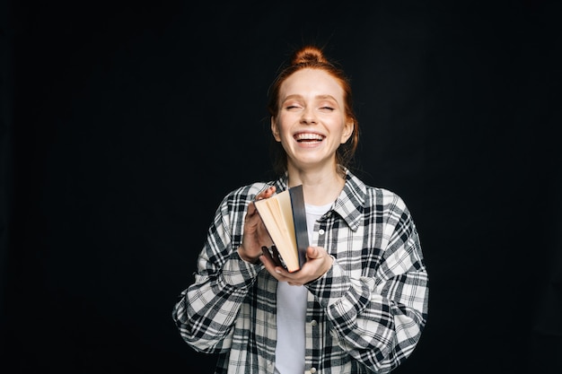 Laughing young woman college student standing holding livre ouvert sur fond noir isolé