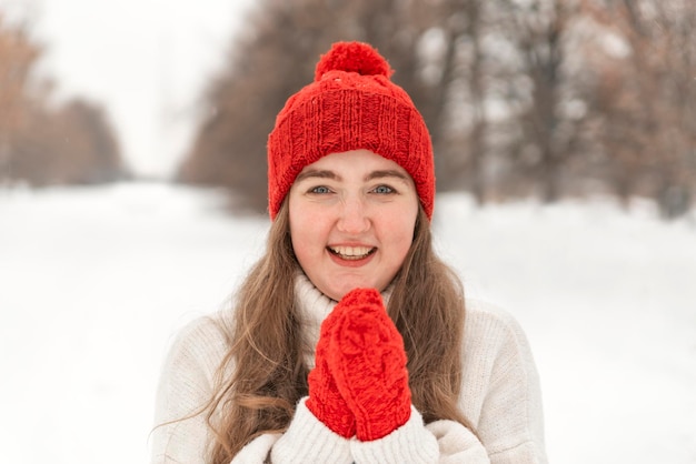 Laughing young woman in red hat tricoté et mitaineswinter park Femme se réchauffe dans des vêtements de laine à l'extérieur par temps froid