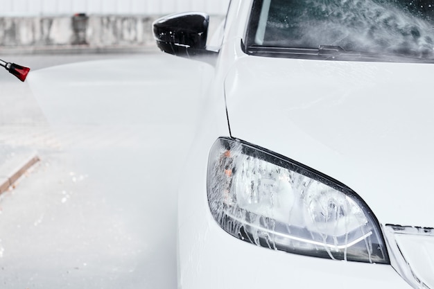 Lavage d'une automobile électrique blanche dans de l'eau à haute pression au lavage de voiture manuel. Concept de service de nettoyage