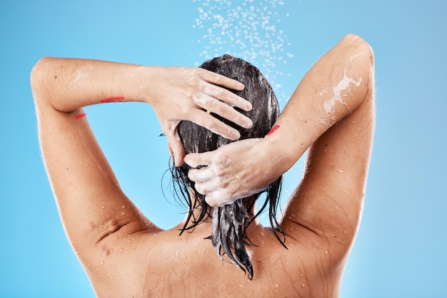 Lavage des cheveux et femme sous la douche avec de l'eau pour le nettoyage et la santé des cheveux sur un fond de studio bleu Nettoyage et hygiène de la salle de bains pour le toilettage des cheveux avec du shampoing ou du savon pendant la douche