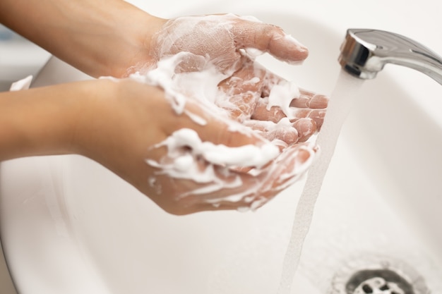 Lavage des mains des enfants avec du savon avec de la mousse abondante sous l'eau courante dans la salle de bain sur un lavabo blanc et robinet chromé