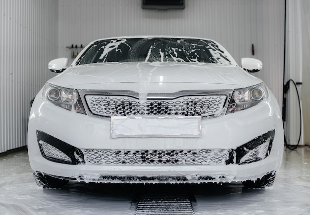 Lavage moderne avec de la mousse et de l'eau à haute pression d'une voiture blanche. Lave-Auto.