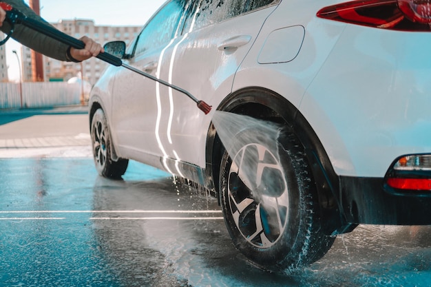 Lavage de voiture manuel avec de l'eau sous pression dans un lave-auto à l'extérieur. Lavage de voiture d'été. Nettoyage de voiture à l'aide d'eau à haute pression. Lavage au savon. Concept de gros plan