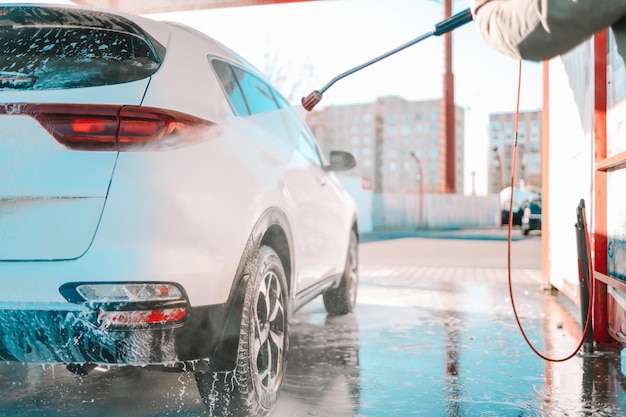 Lavage de voiture manuel avec de l'eau sous pression dans un lave-auto à l'extérieur. Lavage de voiture d'été. Nettoyage de voiture à l'aide d'eau à haute pression. Lavage au savon. Concept de gros plan