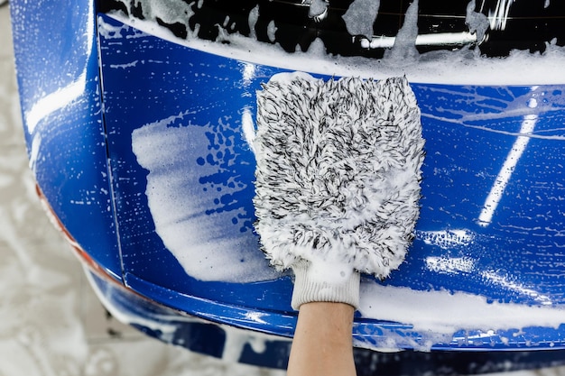 Lave-auto faisant un lavage manuel à la mousse dans un service d'esthétique automobile Lavage des mains avec un gant en microfibre avec une carrosserie en mousse dans le garage