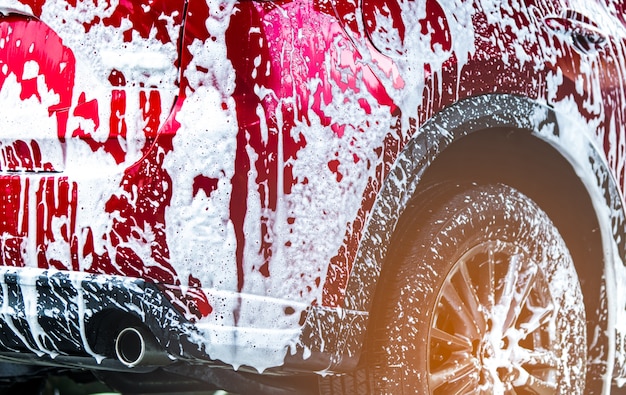 Lave-auto rouge compact SUV avec mousse avant le cirage et le revêtement de verre automobile.