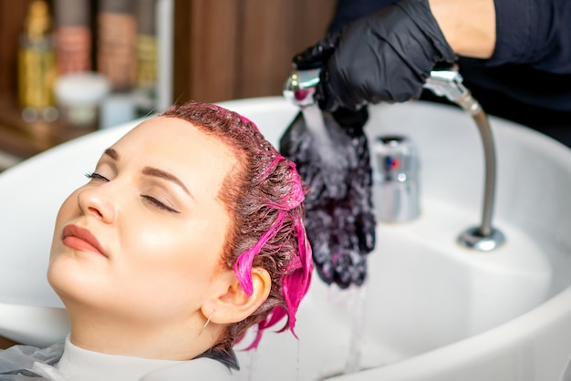 Laver les cheveux des femmes teints. Un coiffeur professionnel lave la peinture de couleur rose d'un client. Jeune femme de race blanche se faisant laver les cheveux dans un salon de beauté.