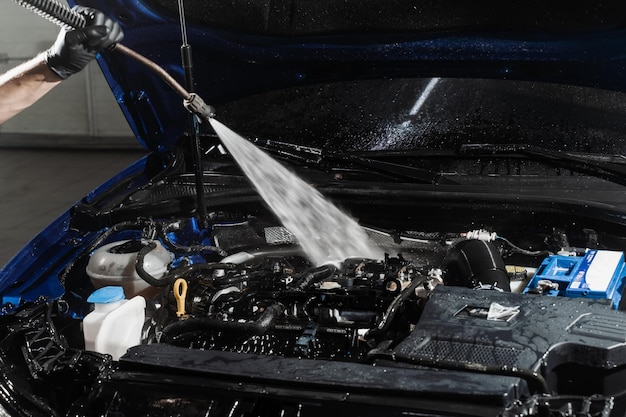 Laver le moteur de la voiture avec de l'eau dans le service automobile de détail Détailler le moteur de nettoyage de la poussière et de la saleté Verser de l'eau sur le moteur de la voiture