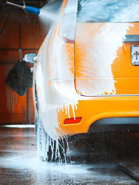 Laver une voiture jaune dans un lave-auto en libre-service sans contact Laver une berline avec de la mousse et de l'eau à haute pression