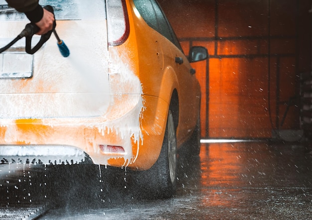 Laver une voiture jaune dans un lave-auto en libre-service sans contact Laver une berline avec de la mousse et de l'eau à haute pression