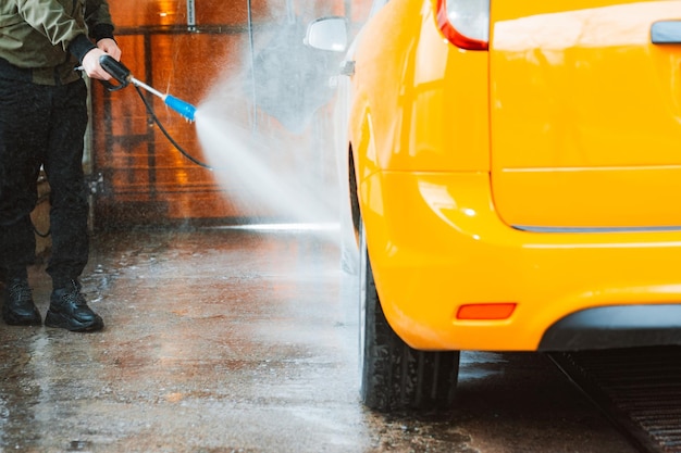 Laver une voiture jaune dans un lave-auto en libre-service sans contact Laver une berline avec de la mousse et de l'eau à haute pression