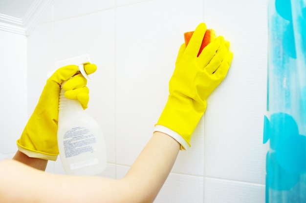 Une laveuse wooman nettoie la surface carrelée dans la salle de bain La fille tient un spray de nettoyage et une éponge dans ses mains Espace de copie