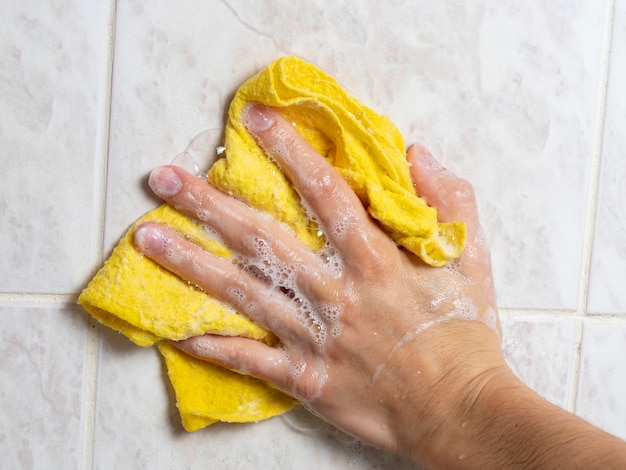 Lavez le carrelage dans la salle de bain avec un chiffon jaune et des produits de nettoyage. Le concept de maintien de l'hygiène à la maison