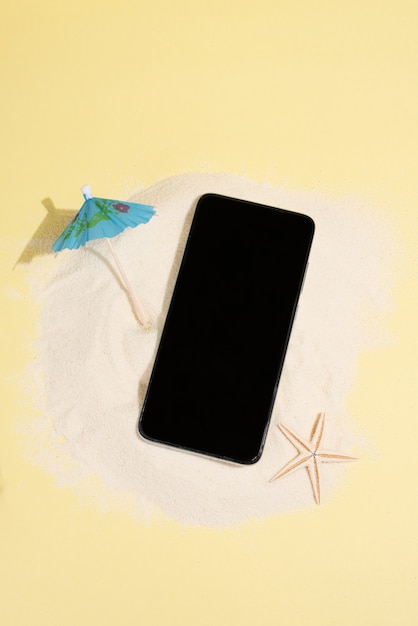 Île de sable avec smartphone, parapluie et étoile de mer sur fond jaune, concept d'été, maquette, gros plan.