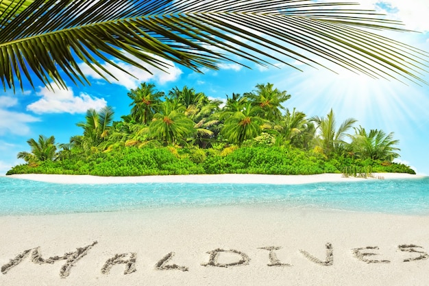 Île tropicale entière dans l'atoll dans l'océan tropical. Île subtropicale inhabitée et sauvage avec des palmiers. Inscription "Maldives" dans le sable sur une île tropicale, Maldives.