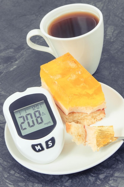 Lecteur de glycémie pour vérifier le niveau de sucre Gâteau éponge sucré crémeux avec gelée et tasse de café Nutrition pendant le diabète Dessert festif
