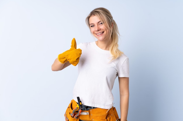 Électricien femme sur mur bleu isolé donnant un geste de pouce en l'air