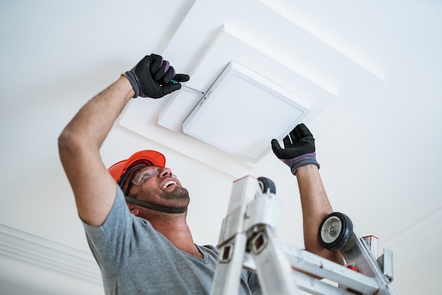 Électricien latino installant une lumière menée au plafond.