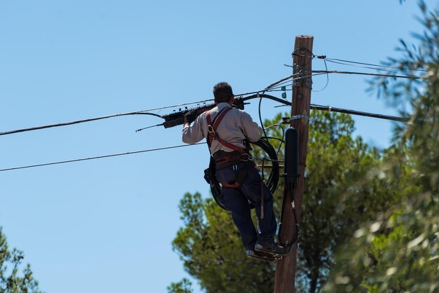 Électricien mâle fixant les fils de la ville au-dessus de la ville sur une échelle avec faisceau