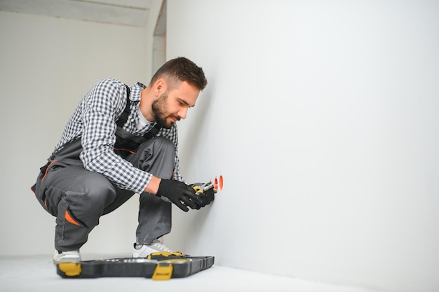 Électricien en uniforme, montage de prises électriques sur le mur blanc à l'intérieur